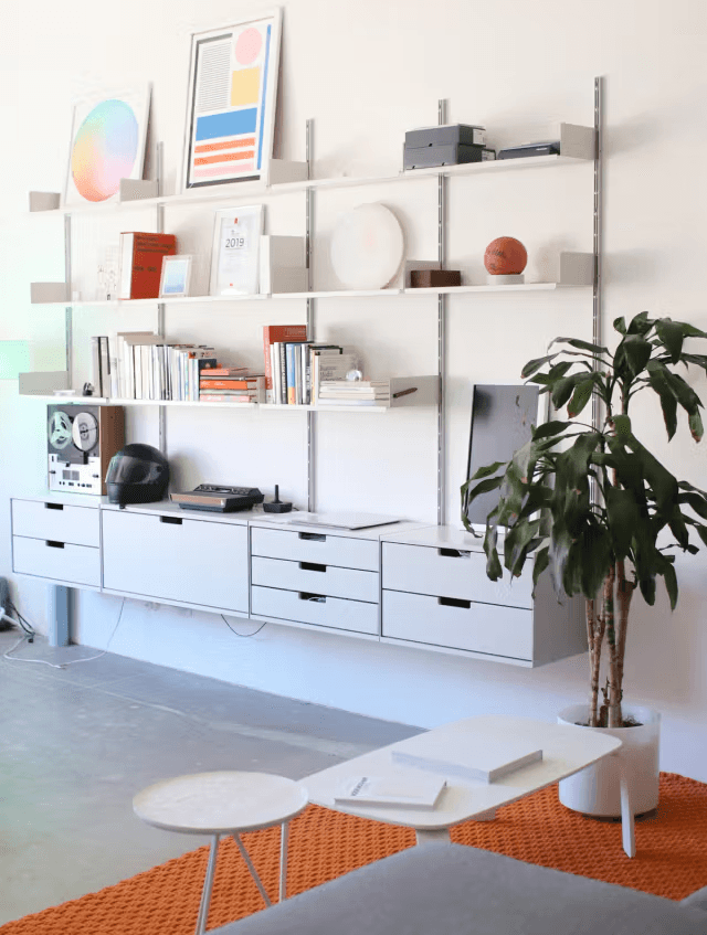 The studio workspace — wall-mounted shelving, art prints, and a potted plant above an orange rug